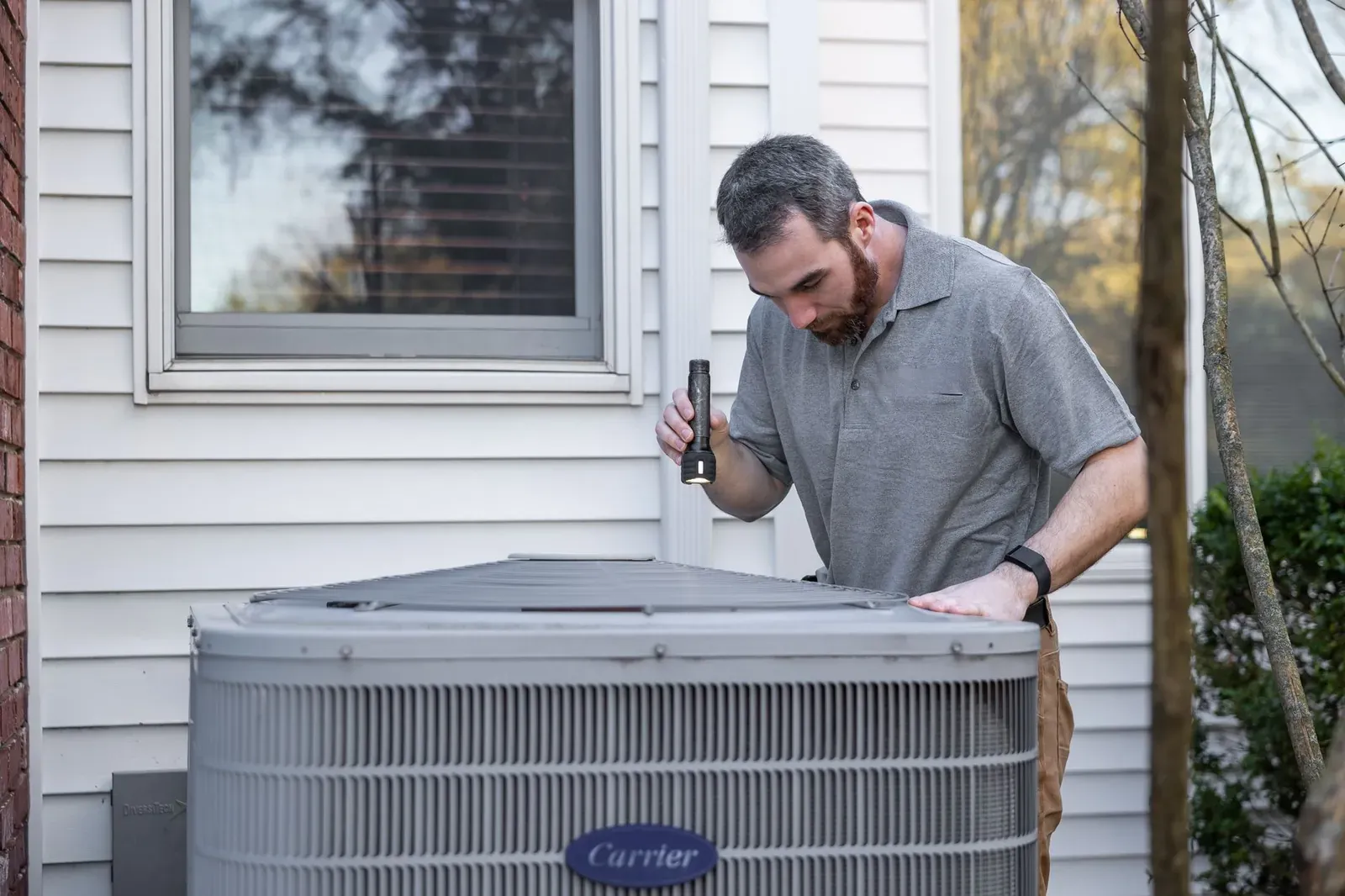 A Brannock technician checking an outdoor air conditioner with a flashlight