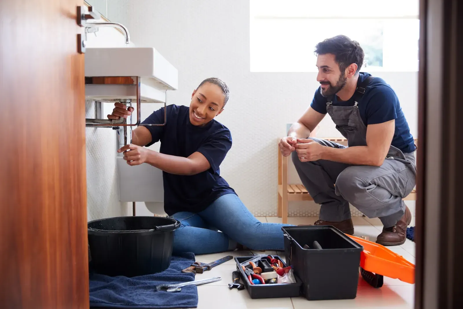 Two Brannock plumbers working under a bathroom sink